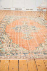 Distressed Oushak rug with faded apricot peach field and blue-green medallion.