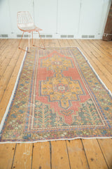 Distressed Oushak rug corner, featuring floral spandrel motifs in pale red, gold, and blue, with fringe.