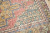 Distressed Oushak rug corner showing faded cinnabar red, gold, and blue geometric floral motifs.