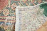 Corner of a distressed Oushak rug, showing muted floral pile and bright green on its woven reverse.
