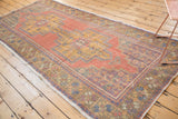 Faded cinnabar red and gold distressed Oushak runner with blue and purple floral motifs.