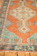 Distressed Oushak rug corner showing burnt orange, mint green, and faded blue stylized border.