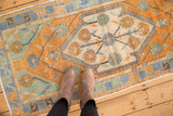 Primitive floral palmettes in faded tangerine, mint, ivory on distressed Oushak rug.