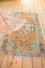 Distressed vintage Oushak rug showcasing faded orange, mint, and blue primitive floral palmettes.