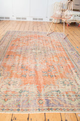 Distressed Oushak rug with faded pistachio, blue, tangerine floral patterns and bottom fringe.