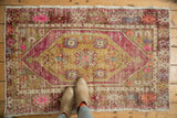 Distressed hand knotted Oushak rug corner, vibrant pink, dusty gold, and purple worn patterns.
