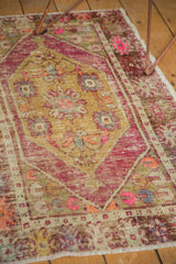 Colorful distressed pile of a vintage Oushak rug, showing gold, pink, and purple medallion motifs.
