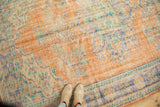 Worn texture of a vintage distressed Oushak rug, featuring apricot and faded blue tones with footwear.
