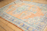 Distressed Oushak rug's faded apricot field with dusty blue and mint green floral motifs.