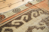 Distressed vintage Oushak runner's textured pile and primitive geometric motifs in terra cotta peach.