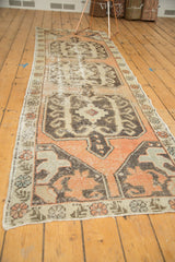 Corner of distressed Oushak runner with faded peach, ivory, and curvilinear tribal motifs.