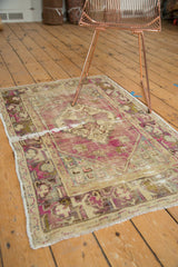 Distressed vintage Oushak rug corner displaying muted purple, beige floral border, and white fringe.
