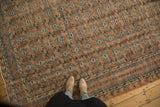 Distressed Oushak rug's faded rust, sky blue, and green floral motifs, seen with feet.