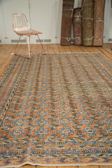 Distressed vintage Turkish Oushak rug with repeating floral gul, terra cotta, blue hues.