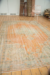 Distressed Oushak rug corner, revealing pale terra cotta, mint green, and foundation wear.