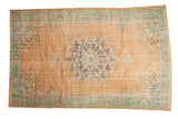 Distressed vintage Oushak rug with faded apricot field and serrated blue-green medallion.