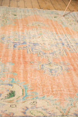 Distressed Oushak rug with faded blush, blue, and ivory tones, revealing worn pile texture.