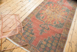 Distressed vintage Oushak runner with geometric medallion in faded cinnabar, blue, and gold.