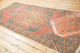 Distressed vintage Oushak runner with faded cinnabar, gold, and dark blue geometric patterns.