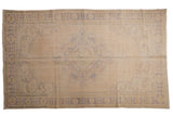 Distressed vintage Oushak carpet, a faded blue scalloped medallion on an open ivory and beige field.