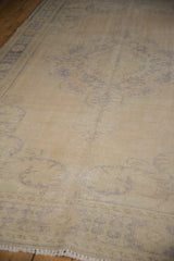 Fringed corner of the distressed Oushak, with faded blue patterns on an ivory field.