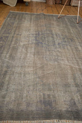 Distressed overdyed Oushak carpet showing woven texture, lazy lines, dark grey, subtle blue.