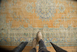 Distressed Oushak carpet with worn texture, faded orange, slate blue, and ivory patterns.