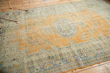 Distressed Oushak carpet corner detail, showing faded floral border, worn orange pile, and selvage.