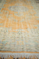 Distressed Oushak carpet end with worn pale burnt orange field, floral motifs, and ivory fringe.