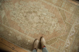 Distressed Oushak rug's soft sand, beige, and faded bronze tones, seen with feet.