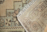 Vintage distressed Oushak rug with low pile, exposed knot heads, woven back, and cream fringe.