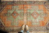 Distressed Oushak rug with geometric double medallions in pale rust and copper green.