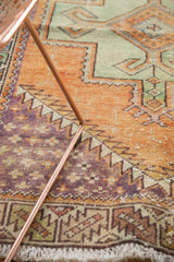 Distressed Oushak rug close-up: geometric border, even wear, rust, green, and purple.