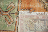 Distressed green and rust pile, original white fringe, and hand-knotted woven foundation of this Oushak rug.