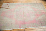 Distressed Oushak rug corner showing pale pink rococo floral patterns, low pile, original selvage.