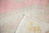 Corner of distressed Oushak rug showing low pink and ivory pile, original selvage, and woven reverse.