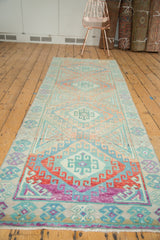 Angled view of a vintage distressed Oushak runner's repeating geometric medallions in pale blush and mint green.
