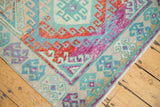 Corner of a distressed Oushak rug showing vibrant hook motifs in gem-like red, blue, and purple.