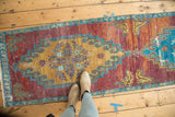Distressed Oushak rug corner showcasing purple, dusty gold, and sky blue geometric medallion fragment with fringe.