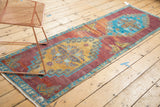 Distressed Oushak runner end, revealing worn pile and foundation beneath blue-gold border.