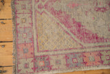 Distressed Oushak rug corner with plum, pink, and dusty gold geometric designs on worn ivory pile.