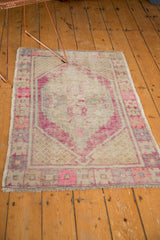 Distressed Oushak rug with vibrant plum medallion, pink borders, and aged ivory field.