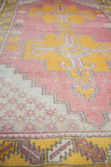 Worn, low pile texture of a distressed Oushak runner featuring raspberry and saffron.
