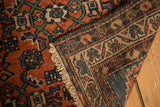 Folded Persian Hamadan rug shows brick red Herati design, detailed border, and tinted fringe.