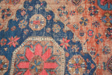 Geometric floral patterns on vintage Soumac rug in blush red, indigo, and aged earthy tones.