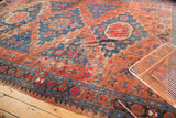 Tattered geometric border and worn brick red and indigo field patterns of an antique Soumac rug.