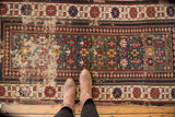Detail of the antique Caucasian rug's teal green field, geometric motifs, and visible wear.