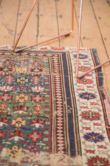 Detail of antique Caucasian rug: worn green field, distinct banded border, and geometric patterns.