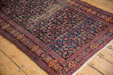 Vintage Senneh rug corner with trident border, Herati field, and visible wear.