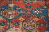 Geometric red and blue panel detail with pile wear on an antique Shirvan rug.